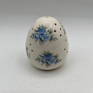May include: White ceramic egg-shaped object with blue floral designs and small holes throughout the surface.