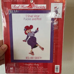 May include: A Red Hat Society counted cross stitch kit. The kit includes a design of a woman in purple and red attire, with the text "I Shall Wear Purple and Red." Finished size is 8" x 10" (20.3 x 25.4 cm).