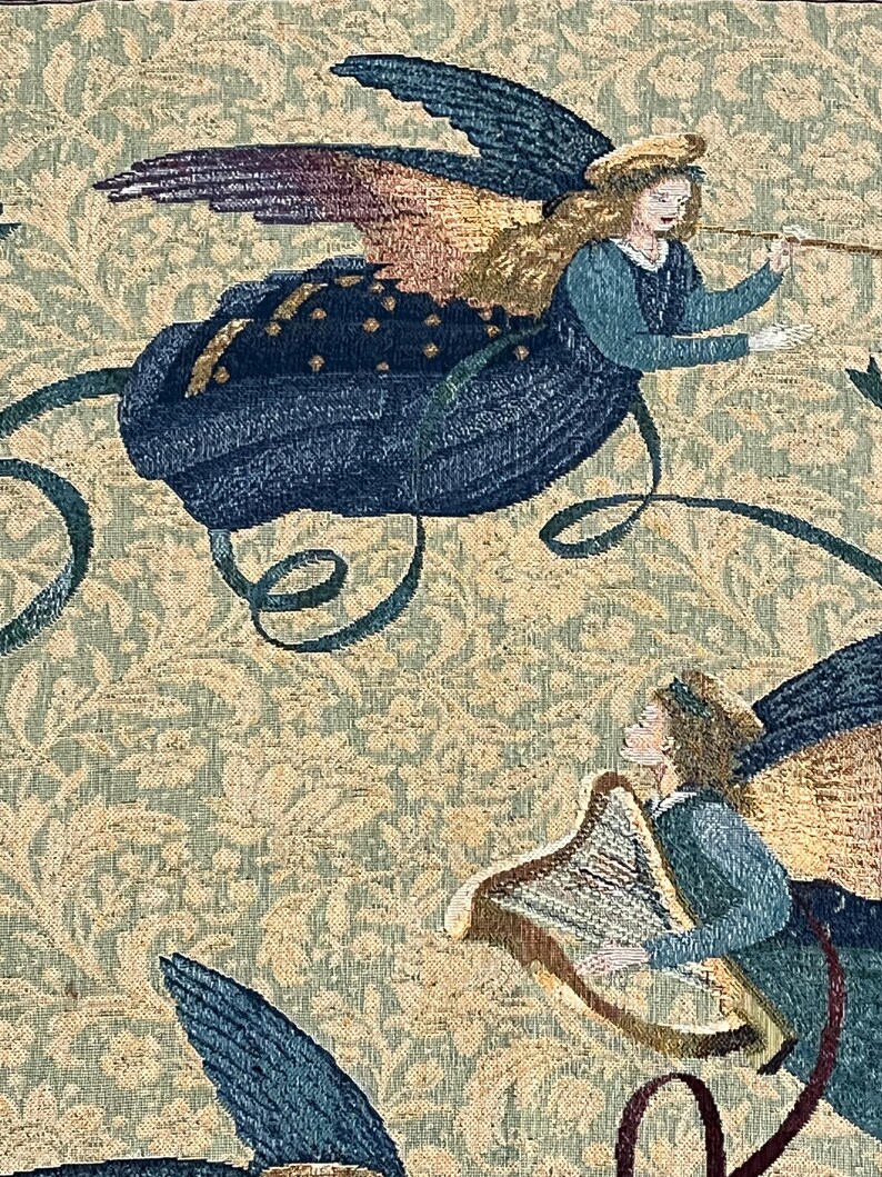 Puede incluir: Tapiz con dos &aacute;ngeles alados, tocando una trompeta y un arpa. Los &aacute;ngeles visten t&uacute;nicas azules sobre un fondo beige con un patr&oacute;n floral. Las alas son una mezcla de azul, dorado y morado.