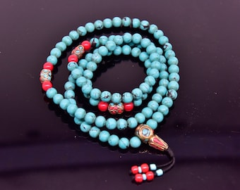 May include: A turquoise and red beaded mala necklace with a gold-toned tassel. The beads are round and have a slightly textured surface. The mala is a traditional Buddhist prayer bead necklace.
