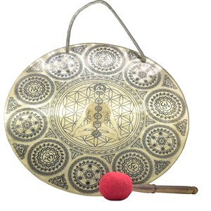 May include: A brass gong with intricate etched designs, including geometric patterns and a central figure in a meditative pose. A red mallet rests beside the gong, ready for use. A rope handle is attached.