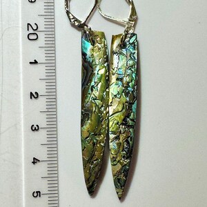 May include: A pair of rectangular earrings with iridescent abalone shell in shades of green, gold, and blue. The earrings are approximately 2 inches long and have silver-colored lever-back closures. The earrings are displayed against a white background.