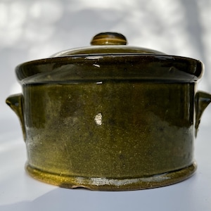 May include: A green ceramic casserole dish with two handles and a lid. The dish has a rustic, handmade look.