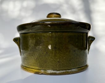 May include: A green ceramic casserole dish with two handles and a lid. The dish has a rustic, handmade look.