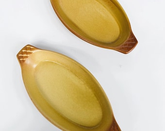 May include: Two yellow ceramic baking dishes with brown handles. The dishes are oval shaped and have a textured surface.