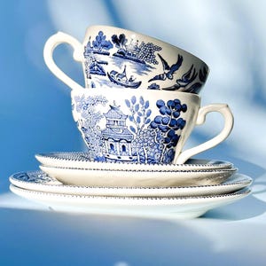 May include: A stack of three white teacups with blue and white floral patterns. The cups are stacked on top of each other, with the top cup's handle facing the right. The cups are on a white saucer.