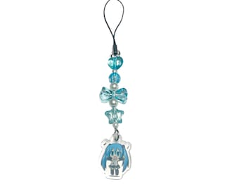 May include: A blue and white beaded charm with a cartoon character pendant. The charm features a black loop, blue beads, a bow, and a star-shaped bead. The pendant is a clear acrylic with a blue-haired anime-style character.