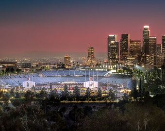 May include: A panoramic view of the Los Angeles skyline at dusk, with the iconic Dodger Stadium in the foreground. The stadium is lit up, with the city lights twinkling in the distance. The sky is a vibrant pink and orange.