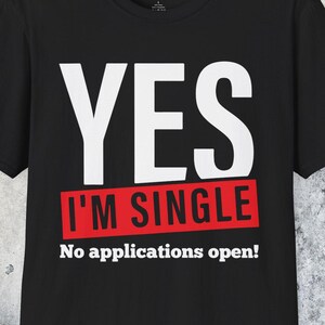 May include: Black t-shirt with the text "YES" in large white letters above a red rectangle that reads "I'M SINGLE". Below, in smaller white letters, it says "No applications open!"