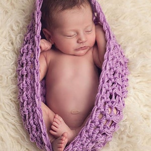 Peut inclure: Un nouveau-né dort paisiblement enveloppé dans une couverture en crochet de couleur mauve. Le bébé est emmailloté dans la couverture, les bras et les jambes repliés. La couverture est faite d'un fil doux et délicat et présente un motif magnifique et complexe.