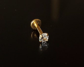May include: A gold-colored stud earring with a clear round gemstone.