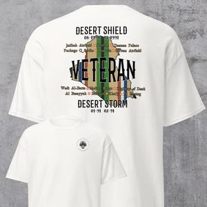 May include: White t-shirt featuring the text "DESERT SHIELD" and "DESERT STORM" with dates. The word "VETERAN" is printed over a map outline. Additional text includes locations. A smaller version of the shirt is visible.