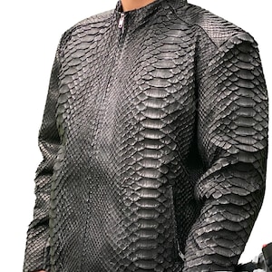 Könnte beinhalten: Schwarze Lederjacke mit Schlangenmuster, Reißverschluss und Stehkragen. Die Jacke wird von einer Person getragen, die neben einem schwarzen und gelben Motorrad steht.