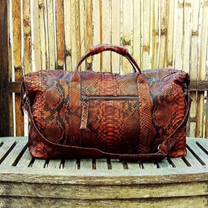 May include: A brown leather duffel bag with a snakeskin pattern. The bag has a top handle and a zipper closure.