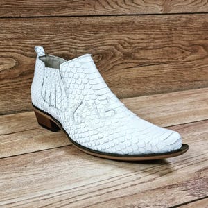 Op de afbeelding: Witte leren cowboylaarzen met een slangenhuidpatroon en een spitse neus.