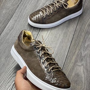 Pode incluir: Ténis de camurça castanho e pele de cobra com atacadores brancos e sola branca.