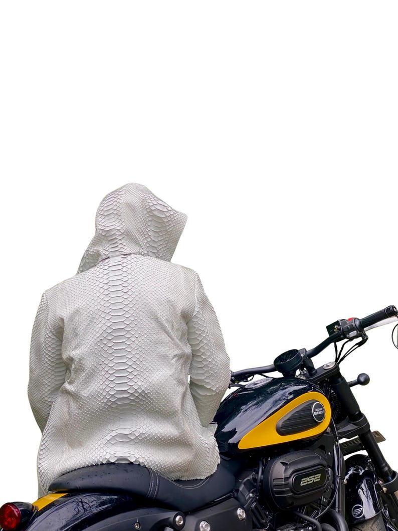 May include: A white, textured hooded jacket with a snakeskin pattern. The jacket is worn while seated on a black and yellow motorcycle. The motorcycle has a black seat and handlebars.