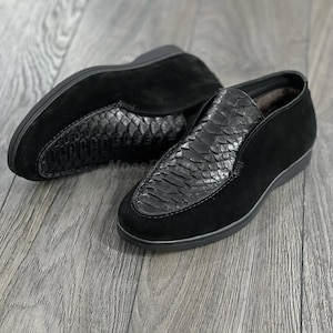 Könnte beinhalten: Ein Paar schwarze Slipper aus Wildleder mit Schlangenhautmuster an der Spitze und einer schwarzen Gummisohle.