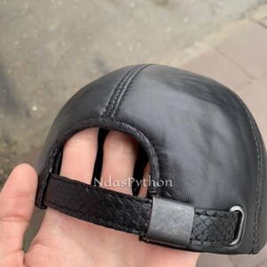 May include: Black leather baseball cap with an adjustable strap and buckle closure.