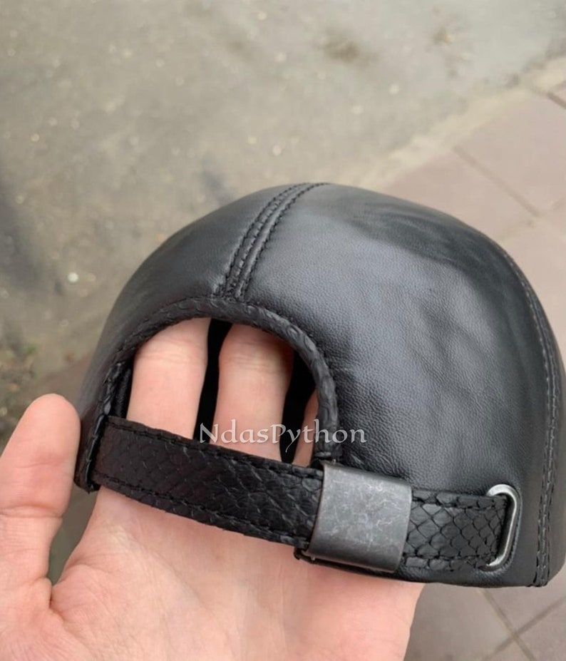 May include: Black leather baseball cap with an adjustable strap and buckle closure.