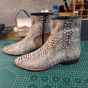 Op de afbeelding: Een paar bruine leren laarzen met een slangenhuidpatroon. De laarzen hebben een spitse neus en een lage hak.