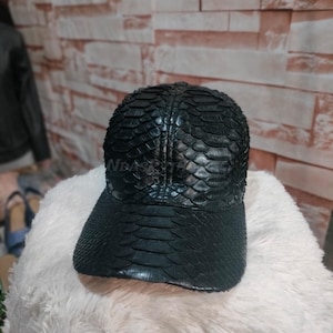 Może przedstawiać: Czarna skórzana czapka z daszkiem z wzorem skóry węża.