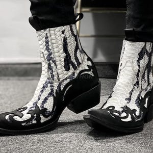 May include: A pair of white and black cowboy boots with a snakeskin pattern. The boots have a pointed toe and a high heel.