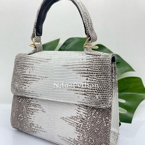 May include: A small white handbag with a black handle and gold hardware. The bag has a textured, snakeskin-like pattern.