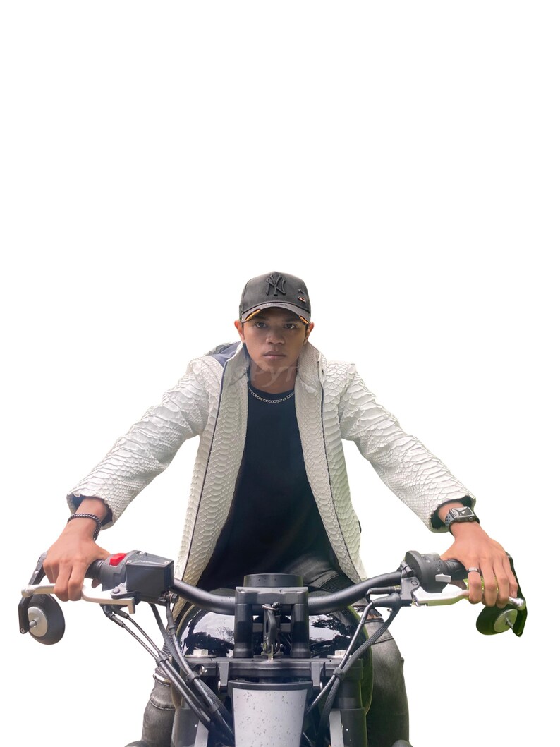 May include: A person wearing a white textured jacket and a black baseball cap, riding a motorcycle. The jacket has a reptile-like pattern. The motorcycle has black handlebars and a black seat.