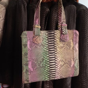 Puede incluir: Un bolso de mano de piel de serpiente multicolor con asa superior. El bolso está hecho de un material texturizado y tiene un esquema de color rosa claro, verde y beige.