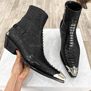 Op de afbeelding: Zwarte leren cowboylaarzen met een spitse neus en zilveren accenten. De laarzen hebben een rits aan de zijkant en een slangenhuidpatroon.