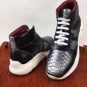 May include: A pair of black high-top sneakers with a snakeskin pattern and white laces. The sneakers have a white sole and a red lining.