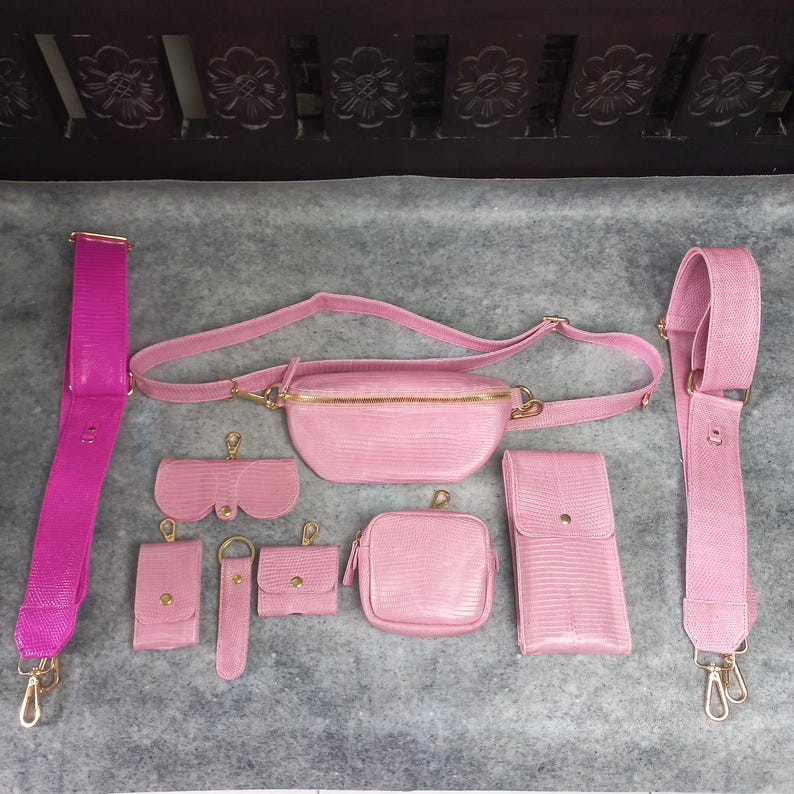 以下が含まれることがあります： ピンク色の革製アクセサリーのコレクション。クロスボディストラップ、ファニーパック、サングラスケース、携帯電話ケース、小さな正方形のポーチ、キーホルダー、小さな財布が含まれます。すべてのアイテムはゴールドトーンの金具を使用しています。
