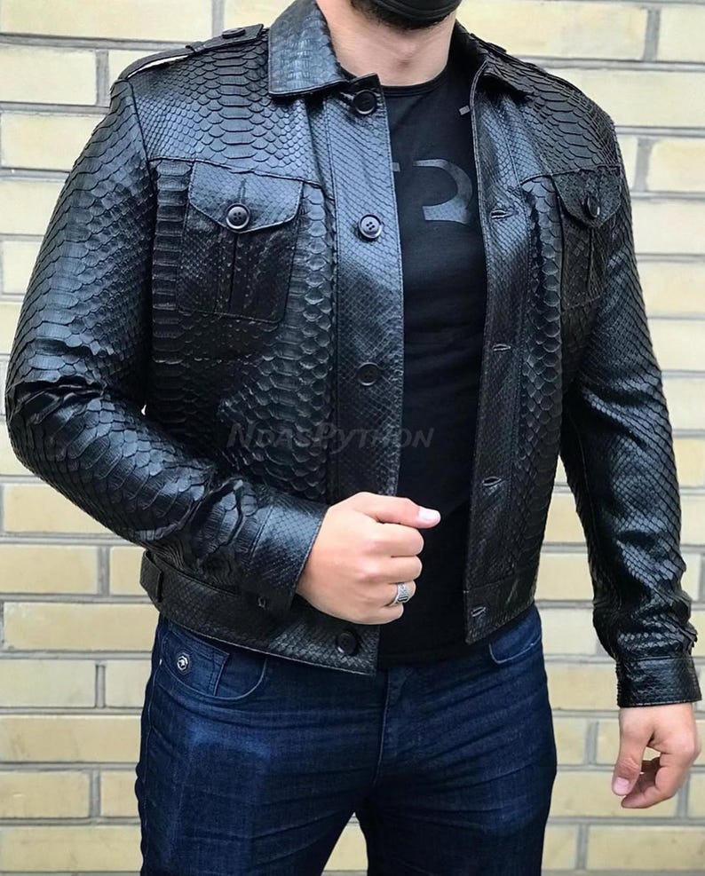 Pode incluir: Uma jaqueta de couro preta com um padr&atilde;o de pele de cobra. A jaqueta tem dois bolsos no peito, bot&otilde;es e gola. A pessoa est&aacute; vestindo uma camiseta preta e jeans azul.