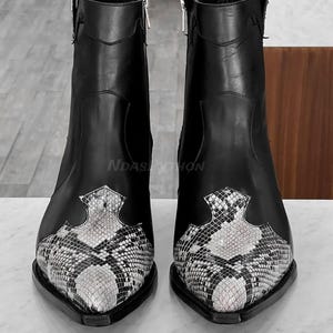 May include: A pair of black leather cowboy boots with a pointed toe and a snakeskin pattern on the front. The boots have a zip on the inside of each boot.