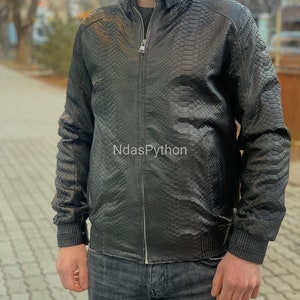 以下が含まれることがあります： ジッパー留めとヘビ柄のブラックレザーのジャケット。ジャケットはスタンドカラーとリブ編みの袖口です。