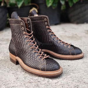 May include: A pair of brown leather boots with a snakeskin pattern and laces. The boots have a thick sole and a rounded toe.