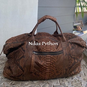 Könnte beinhalten: Eine braune Ledertasche mit Python-Muster. Die Tasche hat einen Reißverschluss und einen oberen Griff.