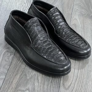 May include: A pair of black leather slip-on shoes with a snakeskin pattern on the toe.