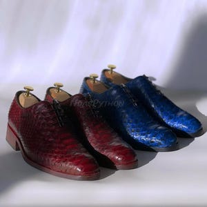 Pode incluir: Três pares de sapatos de couro para vestir com padrão de pele de cobra. Os sapatos são em tons de azul e bordô. Os sapatos são de cadarço e têm bico fino.