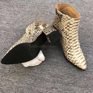 Puede incluir: Botines con estampado de piel de serpiente en tonos beige, marrón y negro. Tienen punta afilada, tacón cuadrado y cremallera lateral. El tacón mide aproximadamente 7,6 cm.