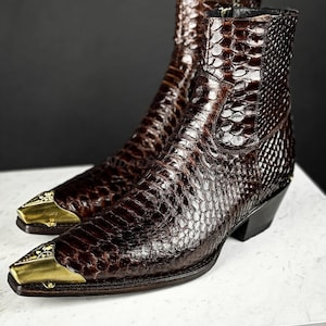 Könnte beinhalten: Braune Leder-Cowboystiefel mit Schlangenhautmuster und goldfarbenen Zehenkappen.