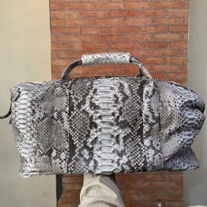 May include: A gray and white snakeskin duffel bag with a top handle.