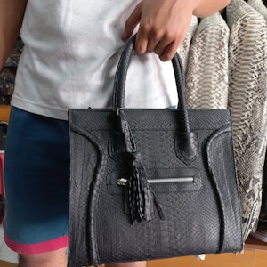 May include: A black leather handbag with a snakeskin pattern and a tassel. The bag has a zippered pocket and a top handle.