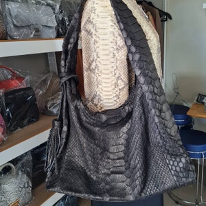 May include: A black snakeskin leather handbag with a long strap. The bag has a textured, scaly pattern and a fringe detail.