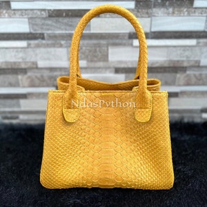 May include: A small, yellow handbag made of python skin with a top handle. The bag has a textured, scaly surface and a subtle sheen.