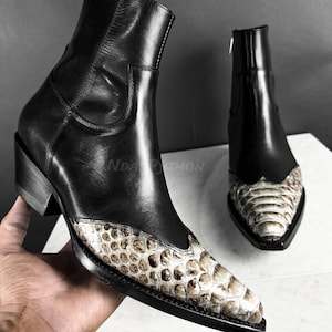 May include: Black leather cowboy boots with a pointed toe and a snakeskin pattern on the front. The boots have a zip on the side and a small heel.
