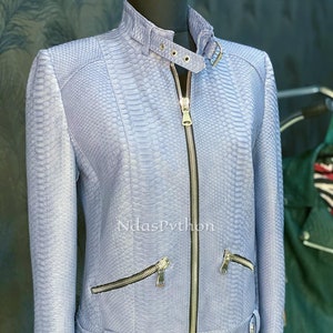 以下が含まれることがあります： 蛇柄のライトブルーの革ジャンパー。ジッパー留めと、前面にジッパー付きポケットが2つ、ウエストにベルトが付いています。