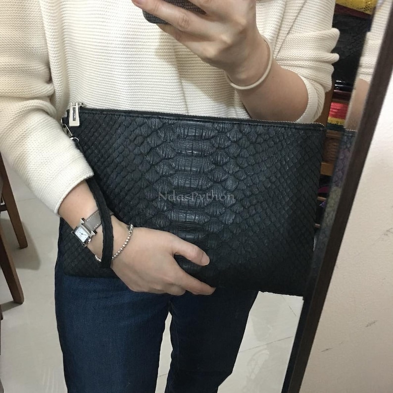 May include: Black clutch with a snakeskin pattern and a wrist strap. The text "NdasPython" is visible on the front of the clutch. The clutch has a zipper closure and a silver-colored zipper pull.