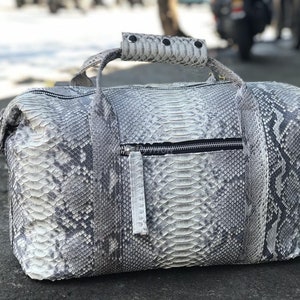 May include: A gray snakeskin leather duffel bag with a zippered pocket and a top handle.